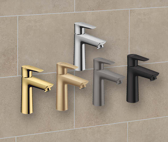 Fünf moderne Badarmaturen in verschiedenen Ausführungen - Gold, Silber, gebürstetes Nickel, mattes Schwarz und Rotguss - stehen vor einer beige gefliesten Wand in einer modernen Hamburger Neubauwohnung.