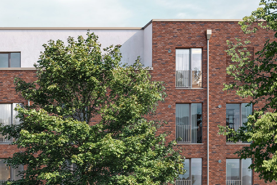 Rote Klinkerfassade mit zurückgesetzem Staffelgeschoss in Hellgrau, bodentiefe Fenster mit Absturzsicherung und 2 von 4 Eichen.
