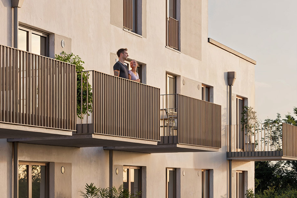 Zoom an einen Balkon mit anthrazitfarbenen Stabgeländer. Menschen schauen in die Abendsonne.