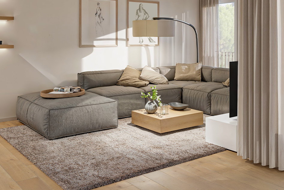 Blick in den Wohnbereich einer Eigentumswohnung mit gemütlichen Sofa und einem Boden mit einer Landhausdiele im Vordergrund.