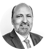 Ein Mann mittleren Alters mit kurzen Haaren und Bart, der einen Anzug, ein Hemd und eine gemusterte Krawatte trägt, lächelt in die Kamera vor einem schlichten, hellen Hintergrund, der den professionellen Geist Hamburgs einfängt.