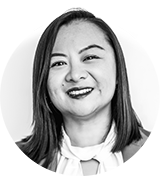 Eine Frau mit glattem, schulterlangem Haar lächelt in einem schicken Blazer und einer Bluse mit Schleife in die Kamera. Aufgenommen in Schwarz-Weiß, verkörpert sie den modernen Geist Hamburgs, der an eine stilvolle Neubauwohnung erinnert.