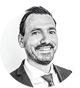 Schwarz-Weiß-Kopffoto eines Mannes in Anzug und Krawatte, lächelnd, mit kurzen dunklen Haaren und leichten Stoppeln, vor einem schlichten weißen Hintergrund - ideal für ein Inserat für eine Neubauwohnung in Hamburg.