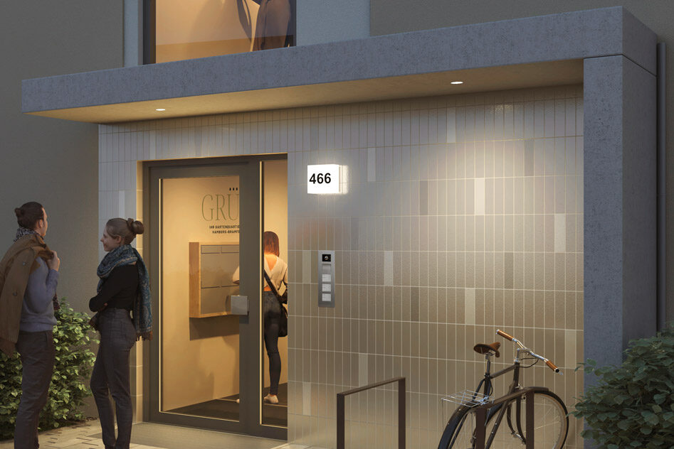 Zwei Personen stehen in der Abenddämmerung in Hamburg vor dem Eingang einer modernen Neubauwohnung und unterhalten sich. Das Gebäude verfügt über eine Gegensprechanlage, die Nummer 466 auf einem Schild, ein in der Nähe geparktes Fahrrad und eine beleuchtete Tür, in der die Buchstaben GRU zu sehen sind.