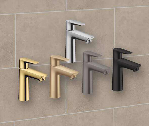 Fünf moderne Badarmaturen in verschiedenen Ausführungen - Gold, Silber, gebürstetes Nickel, mattes Schwarz und Rotguss - stehen vor einer beige gefliesten Wand in einer modernen Hamburger Neubauwohnung.