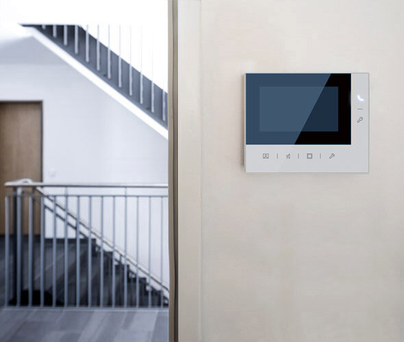 Ein modernes digitales Bedienfeld ist an einer hellen Wand in der Nähe einer Treppe mit Metallgeländer in einer hellen, minimalistischen Neubauwohnung in Hamburg angebracht.