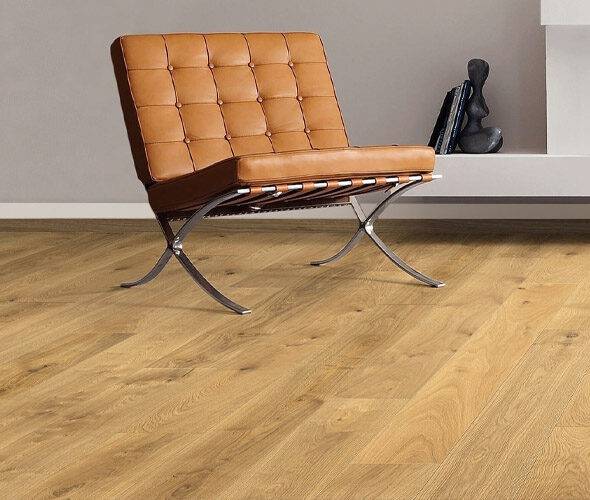 Eine moderne Neubauwohnung in Hamburg mit hellem Holzfußboden, einem hellbraunen Ledersessel mit Metallbeinen und einer schwarzen abstrakten Skulptur auf einem weißen Regal vor einer hellgrauen Wand.