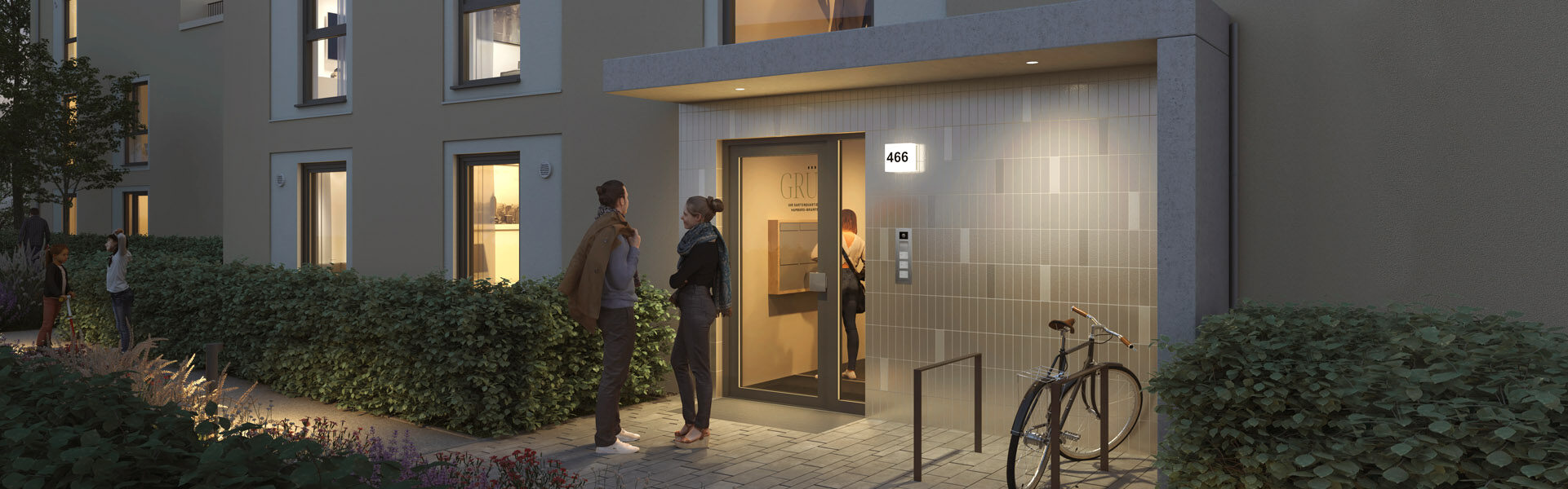 Drei Personen stehen in der Abenddämmerung vor dem schön gestalteten Eingang mit beleuchteter Tür eines modernen Mehrfamilienhauses in Hamburg Bramfeld. Ein Fahrrad ist in der Nähe geparkt, Lichter leuchten aus den Eigentumswohnungen und Sträucher säumen den Gehweg.